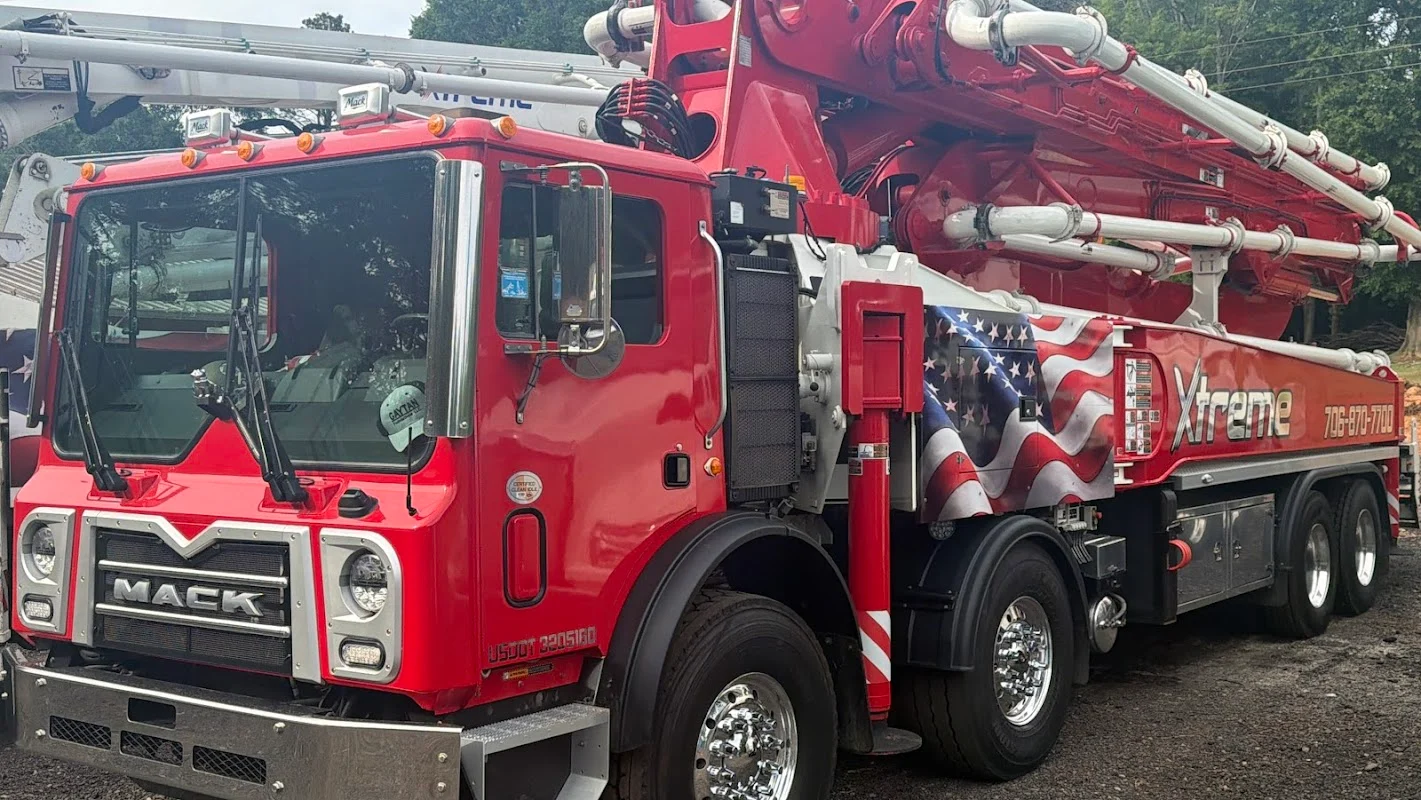 Boom pump truck with extended arm delivering concrete to a residential foundation form.